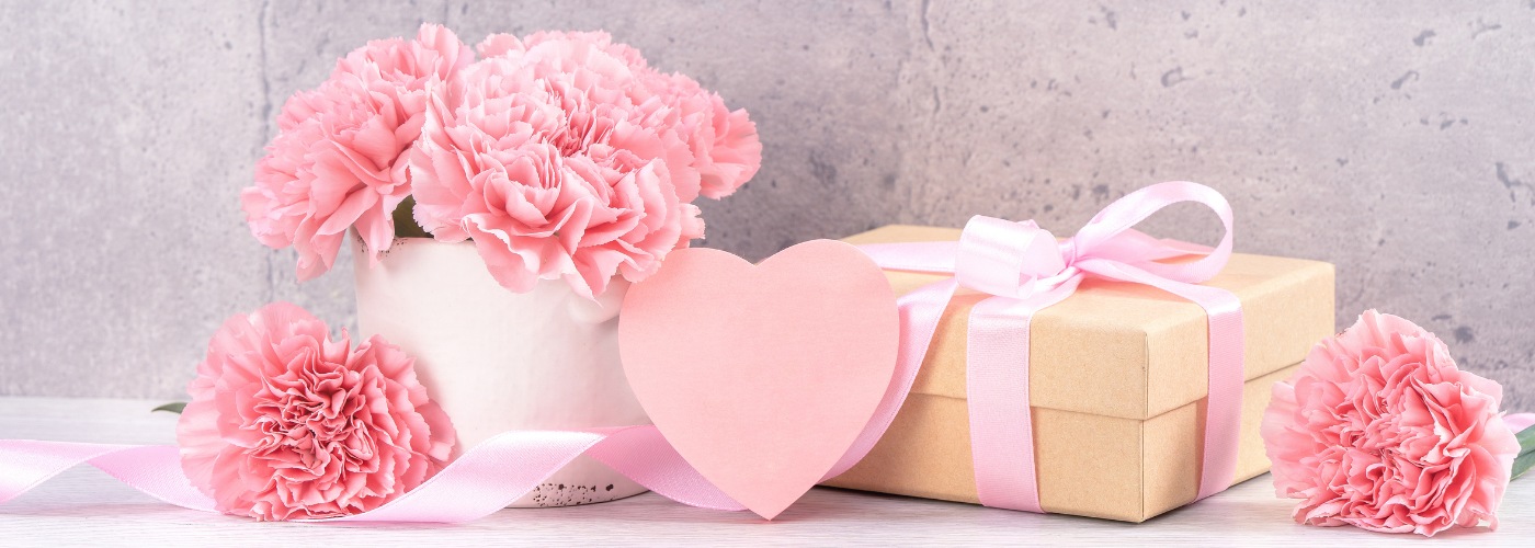 Pink flowers and a gift box with a pink heart in front of them.
