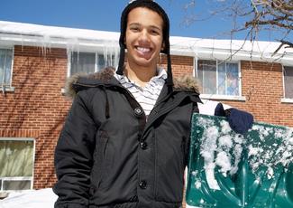 A young man holding a snow shovel and smiling.